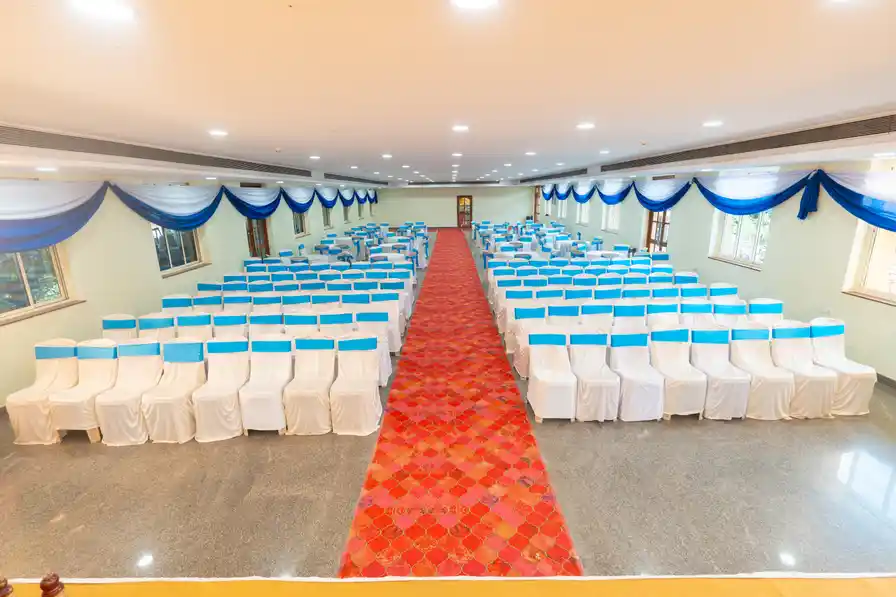 Theatre seating in white chair covers with blue sashes, a red carpet aisle down the middle