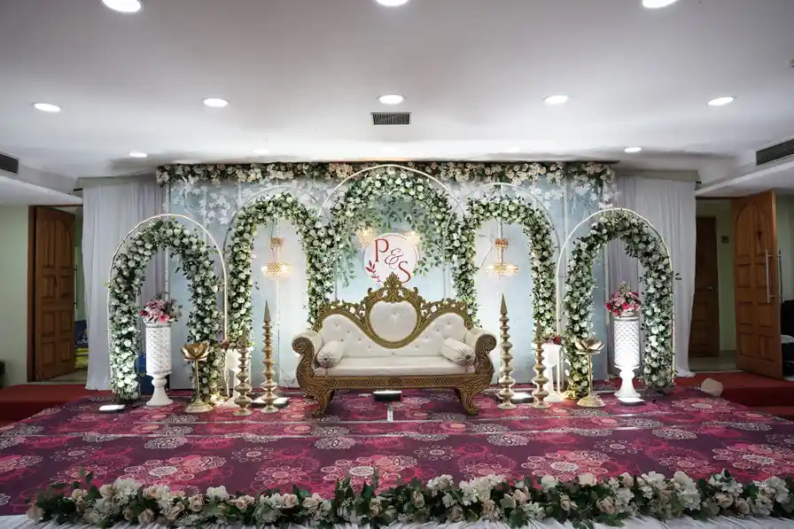 A reception stage framed by floral arches in pink and white, with a settee at the centre