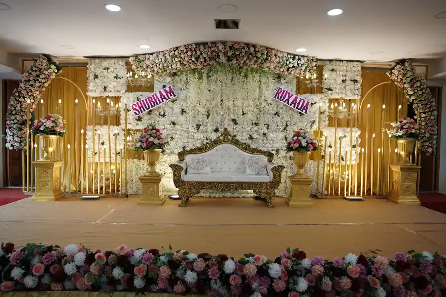 A wedding stage dressed in white and gold florals, with a carved settee and a flower-lined front