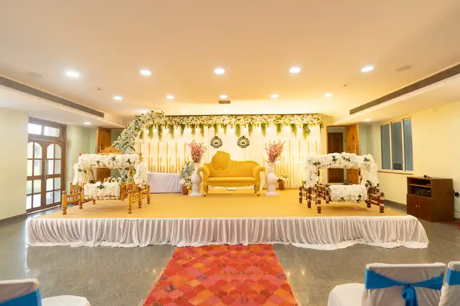 A decorated stage with a gold settee and floral backdrop, red carpet leading to it