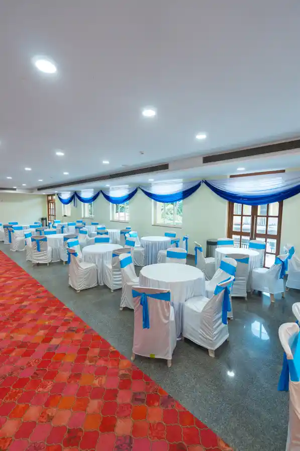 Round tables in white cloths with blue sashes, set for seated dining under blue window drapes