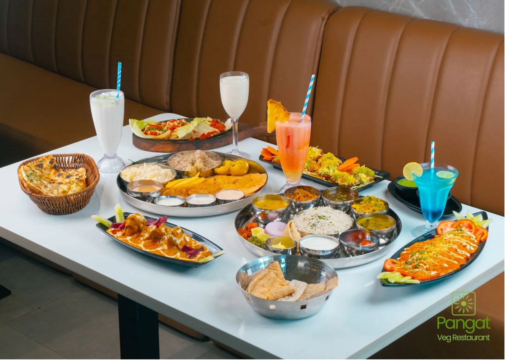 A restaurant table laid with thalis, starters and cold drinks beside a leather banquette