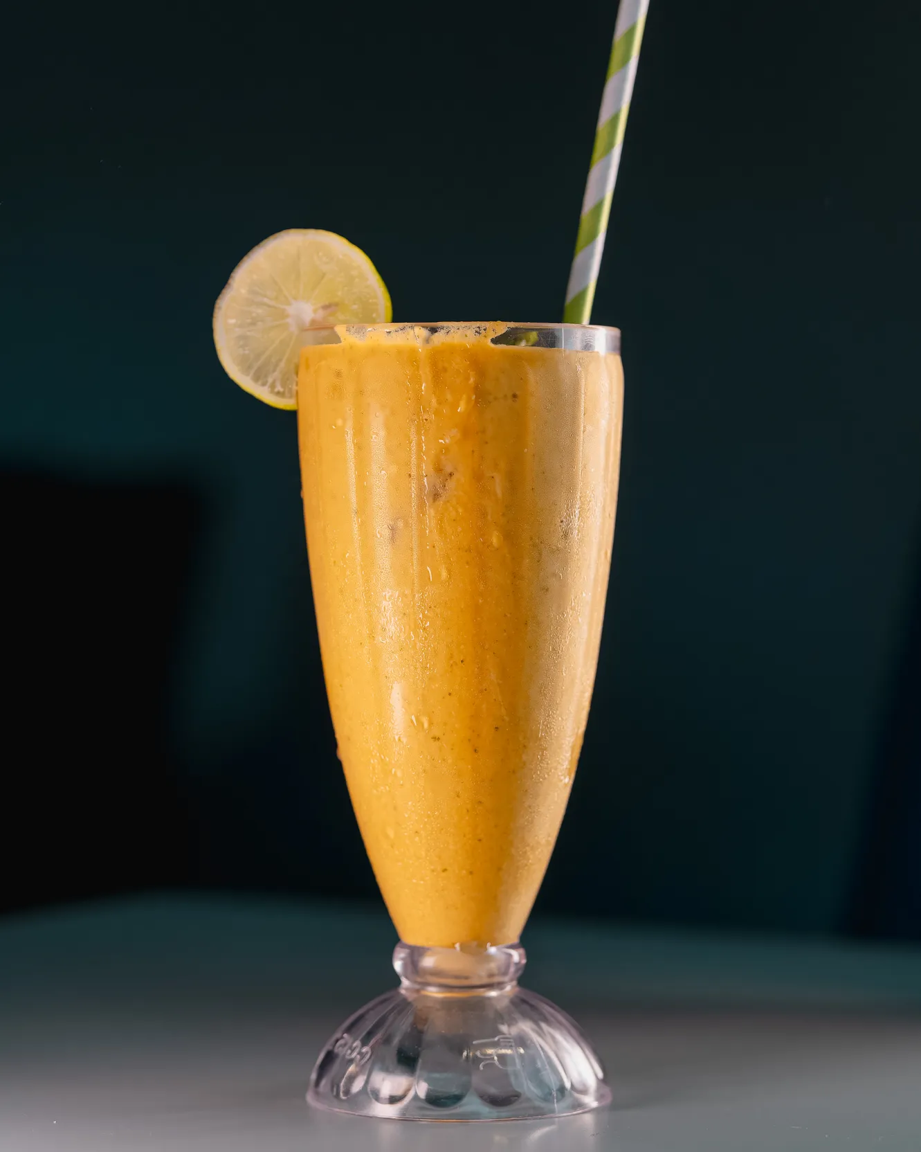 Mango lassi in a tall fluted glass with a lemon slice on the rim