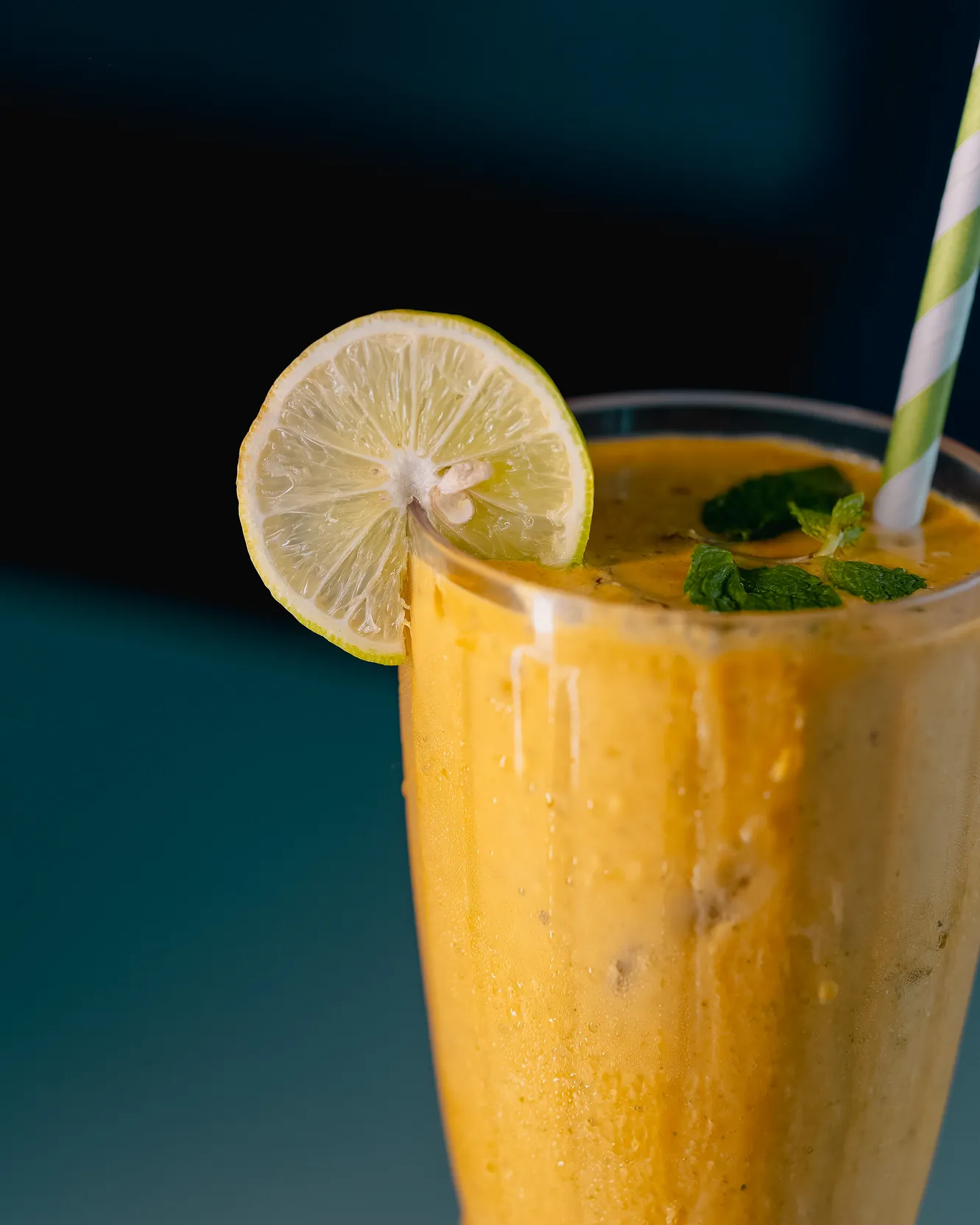 A tall glass of mango lassi topped with a lemon slice and mint
