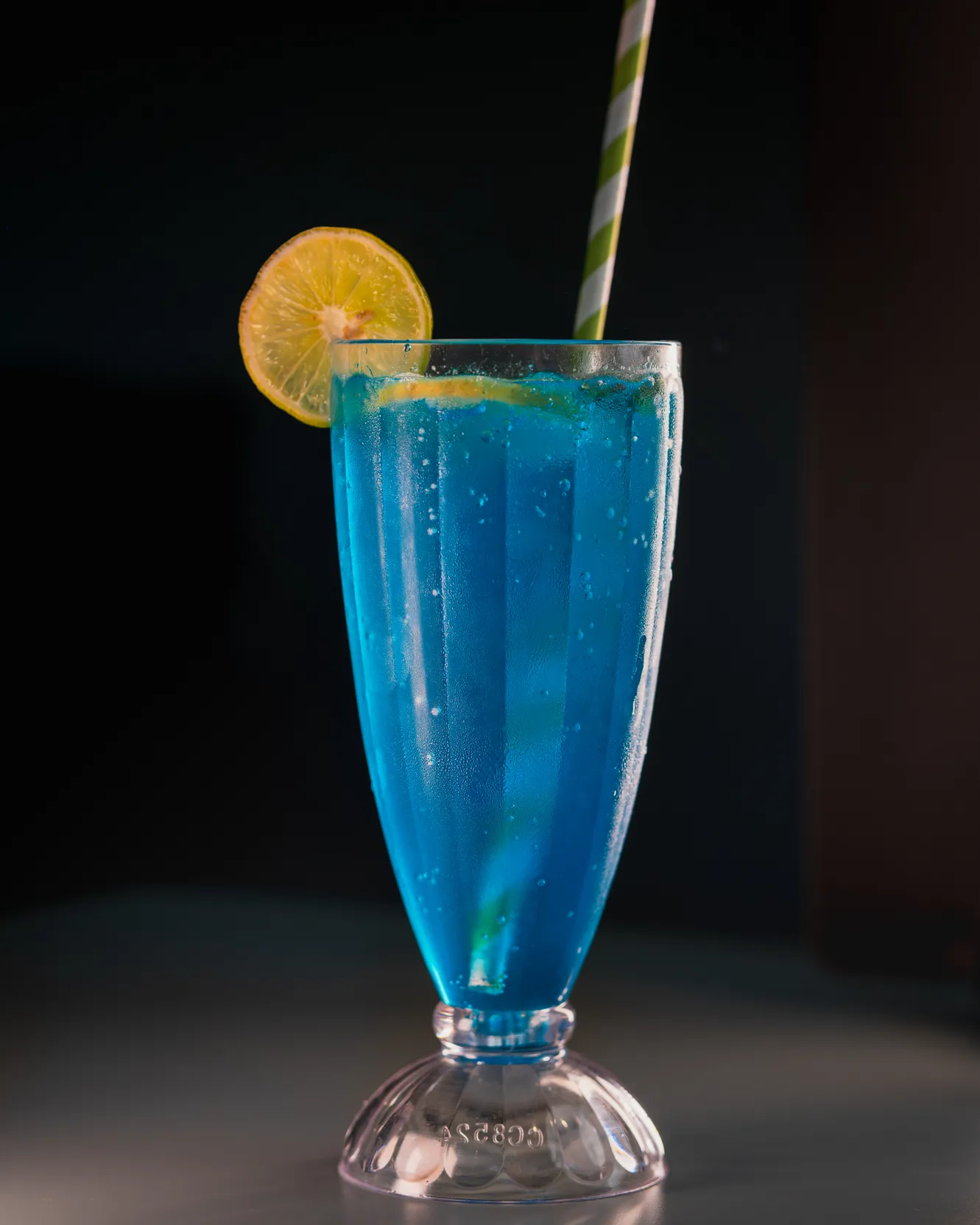 A blue mocktail in a tall fluted glass with a lemon slice on the rim
