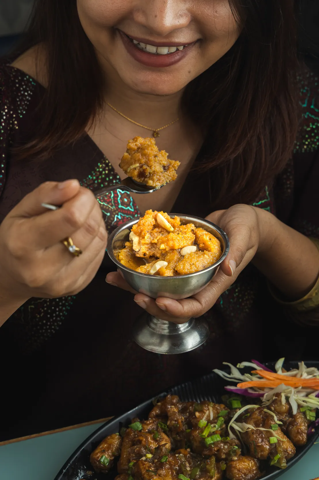 A guest lifting a spoonful from a cashew-topped curry served in a steel bowl