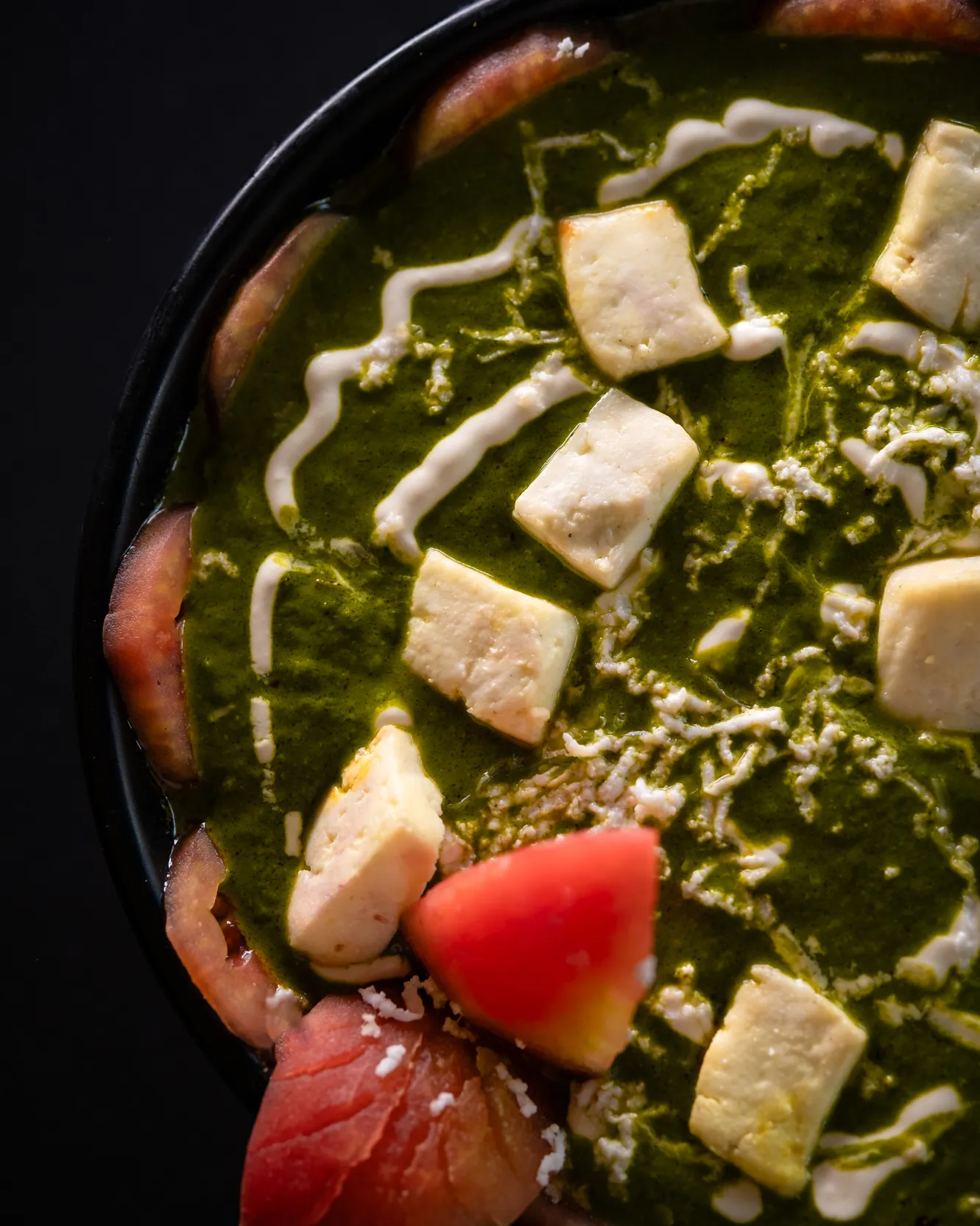 A close view of palak paneer with paneer cubes and tomato wedges