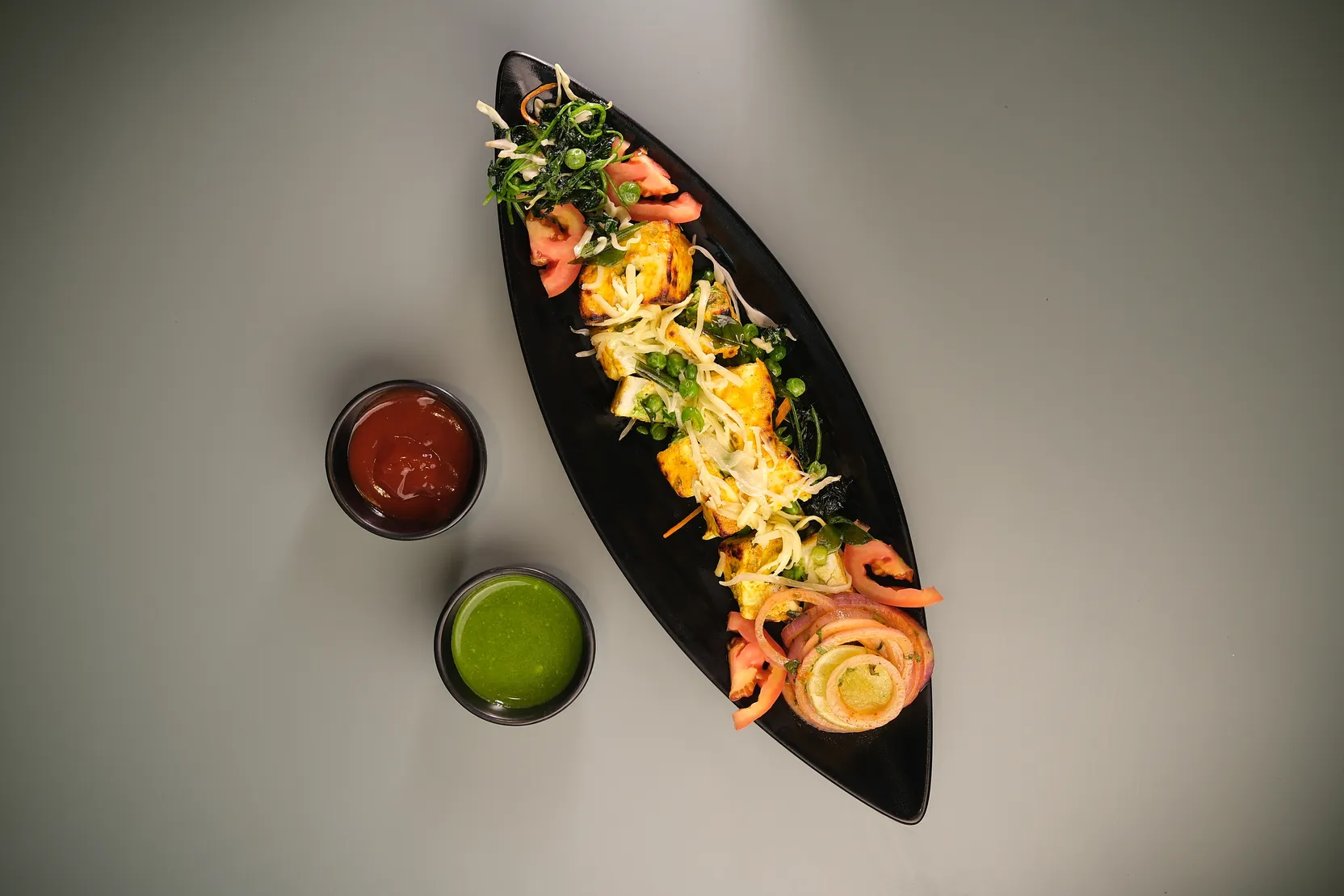 A plated starter on a black boat dish with two dipping sauces