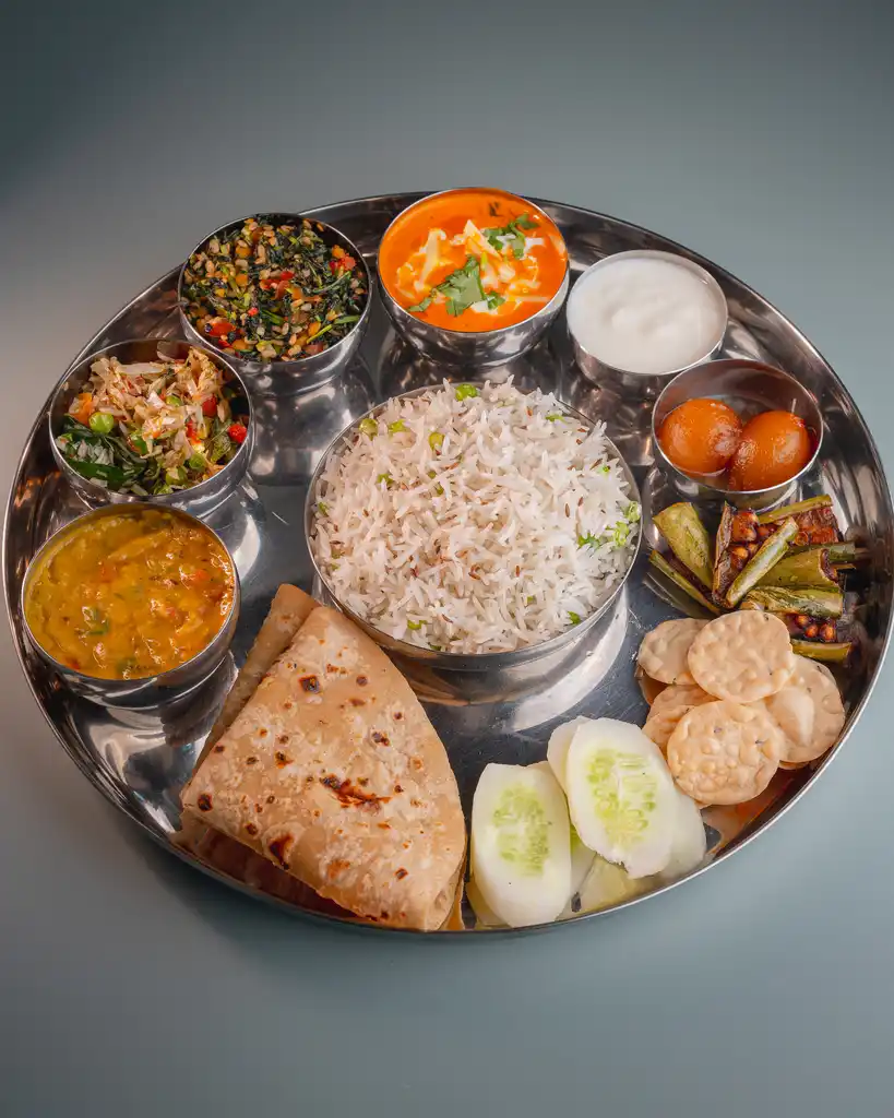 A thali with rice, dal, chapatis, salad, papad and side dishes on a steel plate