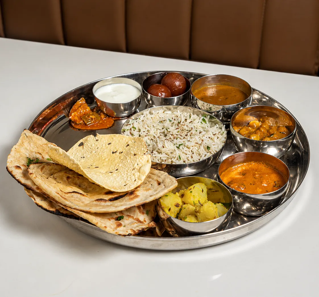 A thali of rice, dal, two vegetables, chapatis, papad and curd on a steel plate