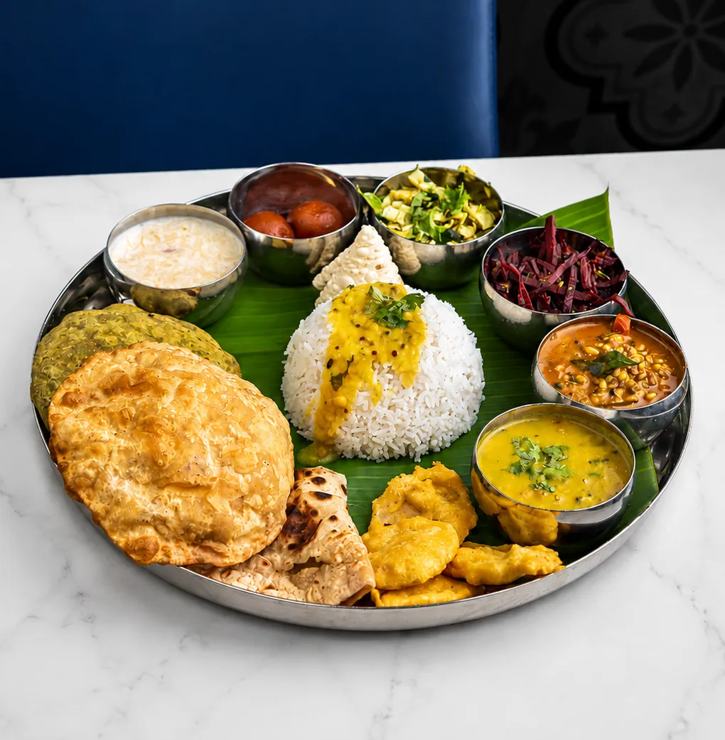 A festive thali on a banana leaf with puris, rice, dal, vegetables and a sweet