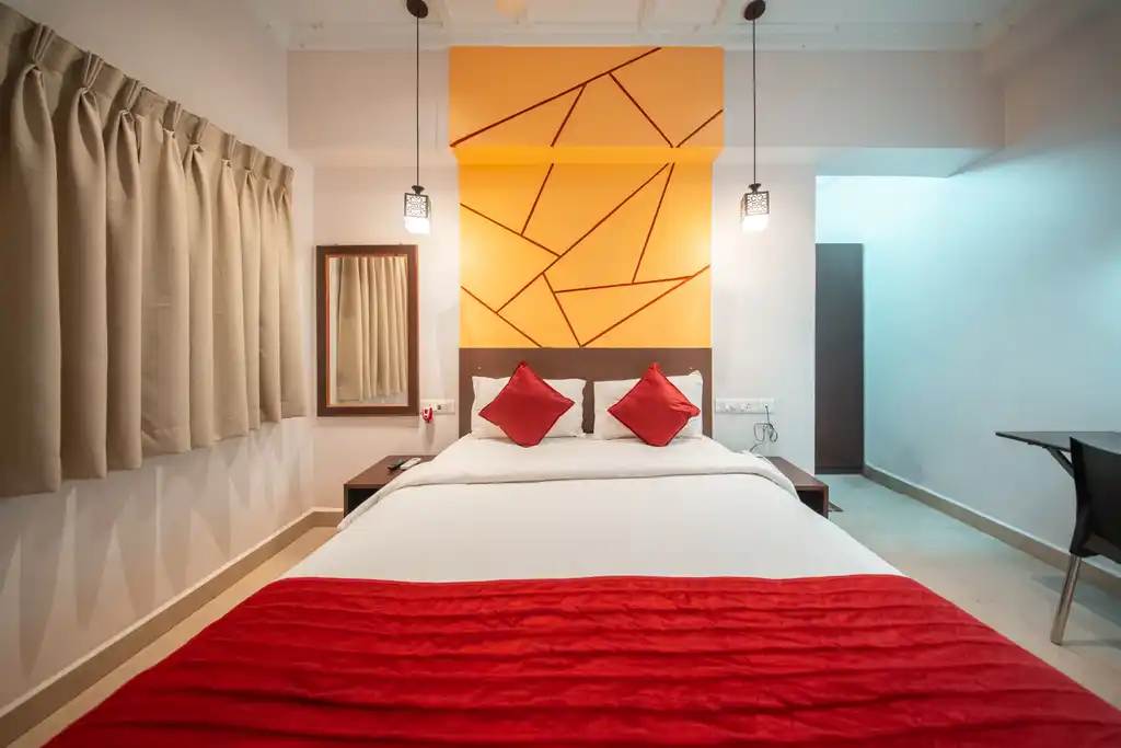 A Deluxe room with a queen bed, red bedspread and pendant lights either side