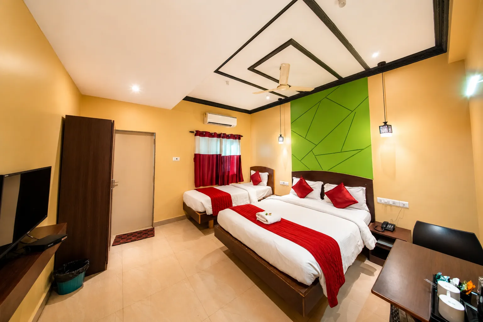 A Deluxe Twin room with three beds, a desk and wardrobe
