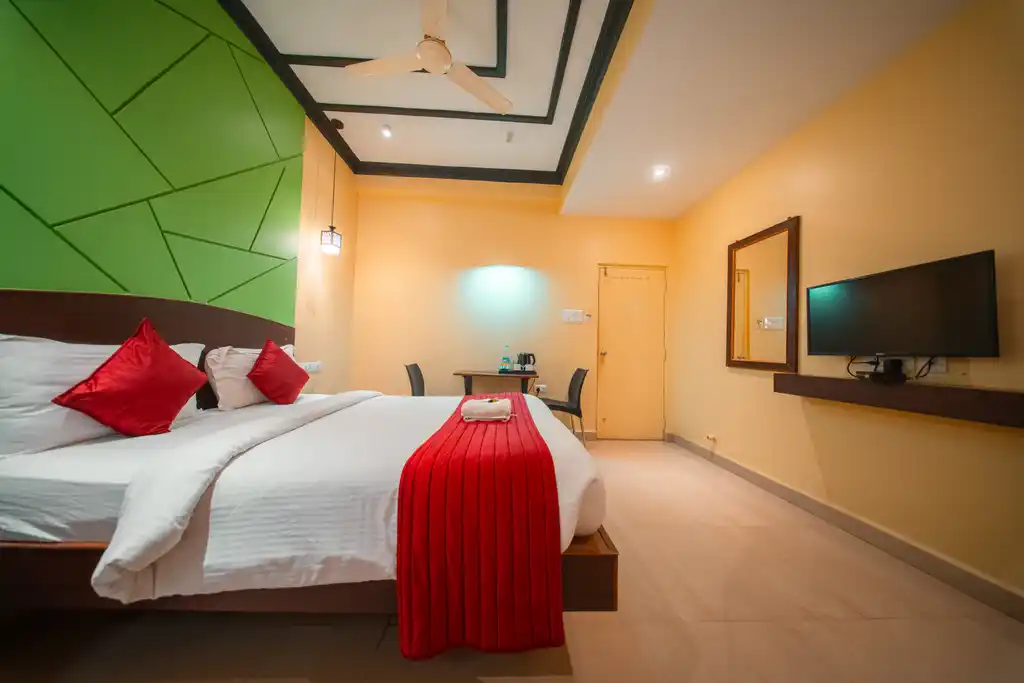 A Deluxe Twin room, beds made up with red runners, beside a wall-mounted television